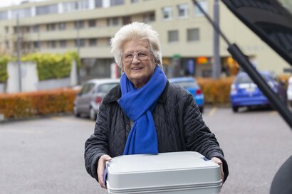 Margrit, freiwillige Fahrerin, im Portrait mit einer Mahlzeitenbox in den Händen